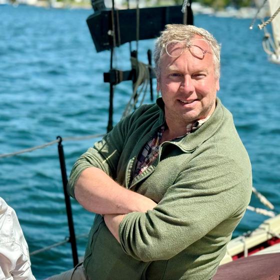Andrew Luke in a green jacket beside the water.