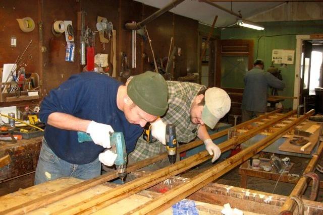 Two of the yard crew working a length of timber on the bench in the woodshop.